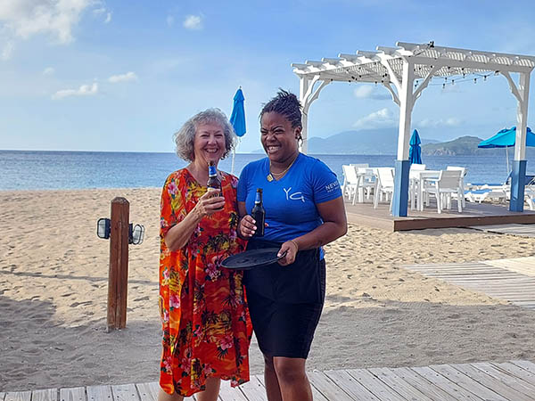 Senior woman with barmaid on the beach at Hamilton Beach Villas and Spa, Nevis, West Indies