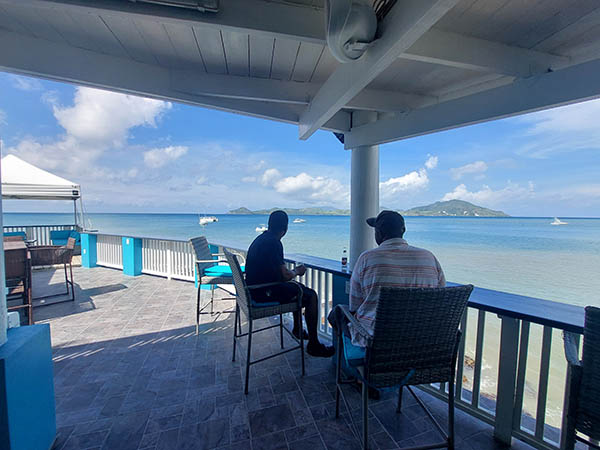 People seated on chairs at the railing overlooking the sea and St.Kitts, from On The Rocks Bar and Lounge, Nevis, West Indies