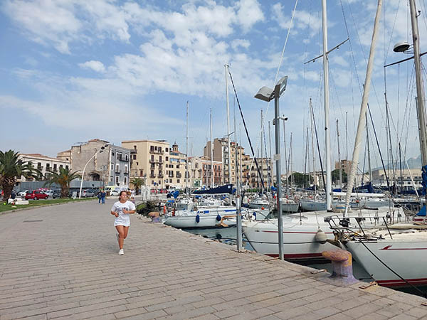 Woman running along waterfront with sailboats in the harbor, Palermo, Sicily