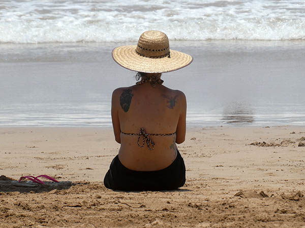 Lady sitting on beach with cell phone and beach hat, Chacala, Mexico