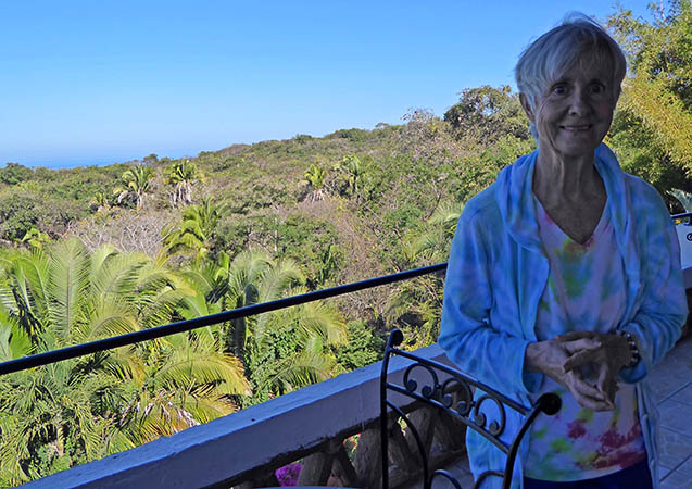 Susana leans against the rooftop railing of her Cafe, with the Chacalilla Bay behind her